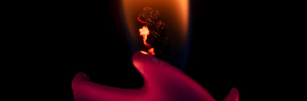 Luz de una vela encendida con un fondo oscuro, mostrando un fuego vibrante y la cera derretida en forma de mano, creando una atmósfera cálida y misteriosa.
