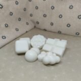 Conjunto de jabones artesanales blancos en diferentes formas sobre una superficie clara, con fondo de tela beige decorada con flores. Ideal para productos de cuidado personal y decoración.