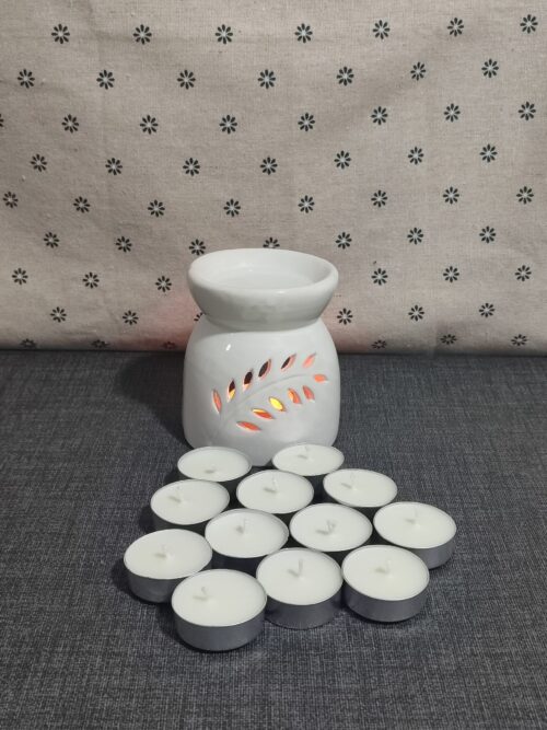 Difusor de cerámica blanca con diseño de hojas, acompañado de velas tipo té. Fondo textil con estampado de flores. Ideal para aromaterapia y ambientación.