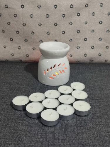 Difusor de cerámica blanca con diseño de hojas, acompañado de velas tipo té. Fondo textil con estampado de flores. Ideal para aromaterapia y ambientación.