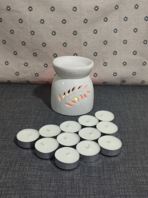 Difusor de cerámica blanca con diseño de hojas, acompañado de velas tipo té. Fondo textil con estampado de flores. Ideal para aromaterapia y ambientación.