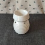 Vaso de cerámica blanca con diseño estriado, ideal para aromatizantes o velas, sobre fondo textil gris.