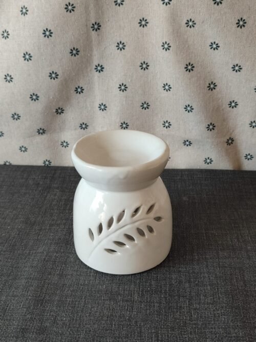 Difusor de cerámica blanca con diseño de hojas, ideal para aromatizar espacios. Fondo textil con estampado de flores.