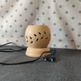 Lámpara de cerámica con diseño de hojas, conectada a un cable eléctrico, sobre una superficie textil gris. Ideal para decoración y aromaterapia.