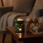 Lámpara de aromaterapia verde con velas encendidas sobre una mesa de madera, junto a un paquete de velas blancas, en un ambiente acogedor y relajante.