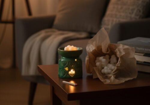 Lámpara de aromaterapia verde con velas encendidas sobre una mesa de madera, junto a un paquete de velas blancas, en un ambiente acogedor y relajante.
