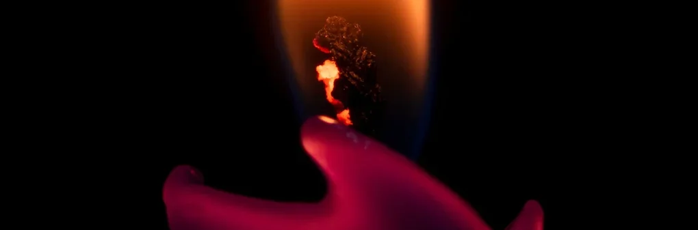 Luz de una vela encendida con un fondo oscuro, mostrando un fuego vibrante y la cera derretida en forma de mano, creando una atmósfera cálida y misteriosa.