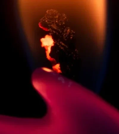 Luz de una vela encendida con un fondo oscuro, mostrando un fuego vibrante y la cera derretida en forma de mano, creando una atmósfera cálida y misteriosa.